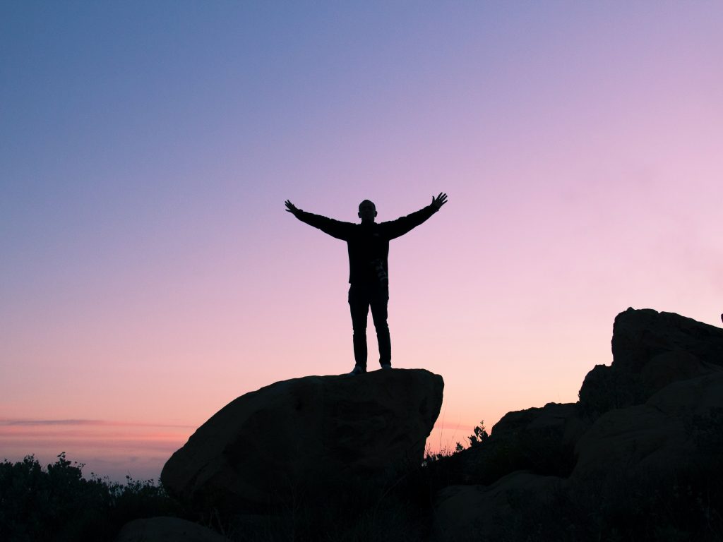 person on top of a rock, silhouetted, arms uplifted