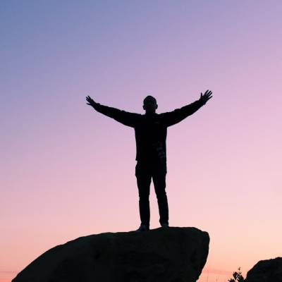 man on a rock at sunset with arms outstretched above head